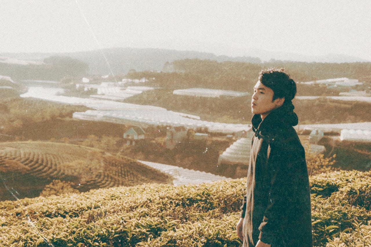 A young man stands thoughtfully overlooking a scenic cropland landscape at sunrise.