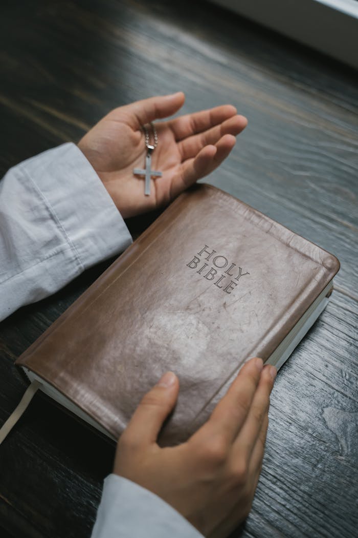 Close-up of hands holding a Holy Bible with a cross necklace, symbolizing faith and spirituality.