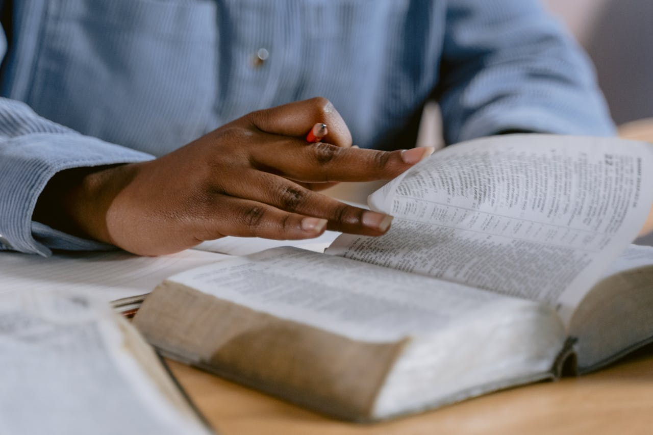 A person wearing a blue shirt flipping through a Bible, highlighting faith and study.